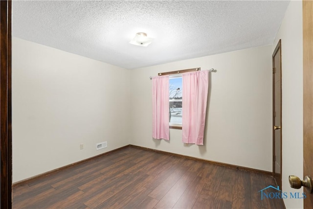 spare room featuring dark hardwood / wood-style flooring and a textured ceiling