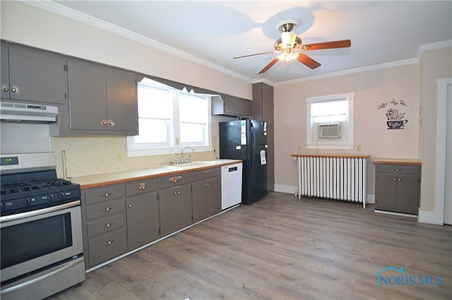 kitchen featuring radiator heating unit, extractor fan, dishwasher, black fridge, and stainless steel gas stove