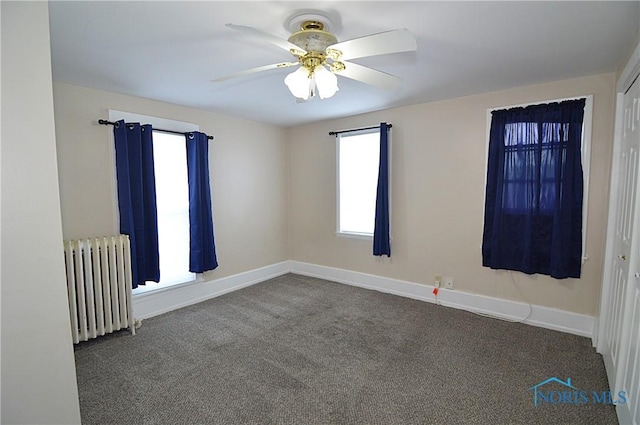 unfurnished room featuring radiator heating unit, ceiling fan, and dark colored carpet