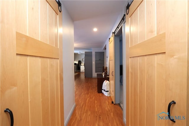 corridor featuring hardwood / wood-style flooring, a barn door, and wooden walls