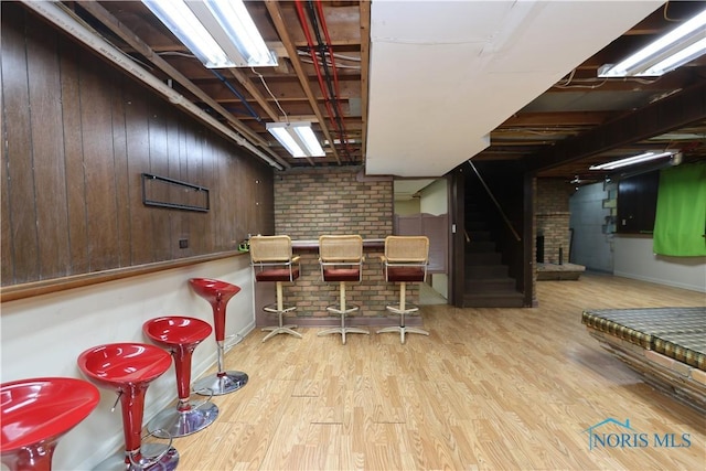 bar with wooden walls, light hardwood / wood-style flooring, and brick wall