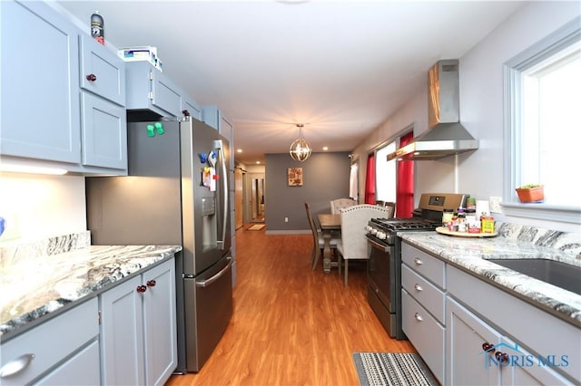 kitchen featuring appliances with stainless steel finishes, light wood-type flooring, wall chimney exhaust hood, decorative light fixtures, and an inviting chandelier