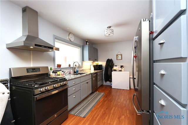 kitchen with sink, stainless steel appliances, wall chimney range hood, hardwood / wood-style floors, and gray cabinets