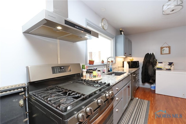 kitchen with gray cabinetry, dark wood-type flooring, sink, stainless steel gas range, and range hood