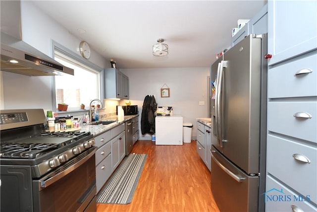 kitchen with wall chimney range hood, sink, gray cabinets, light hardwood / wood-style floors, and stainless steel appliances