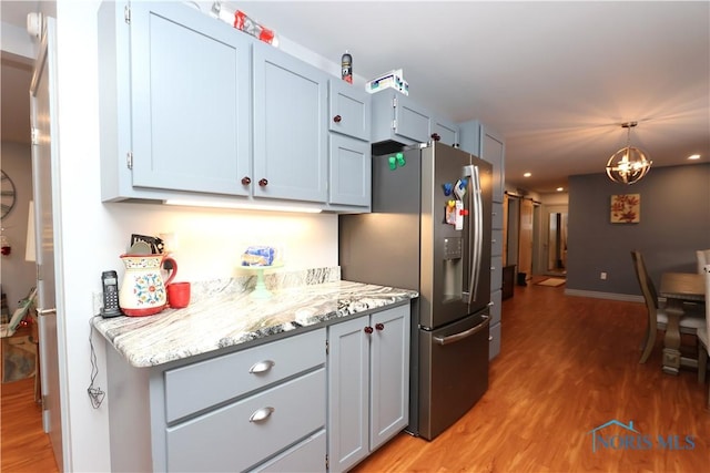 kitchen with light stone countertops, stainless steel refrigerator with ice dispenser, pendant lighting, wood-type flooring, and a chandelier