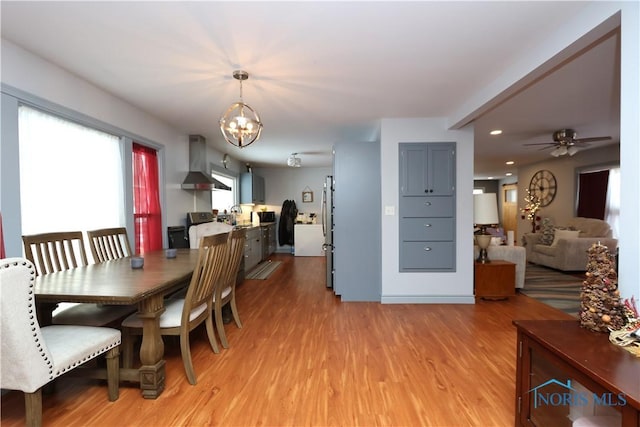 dining space with ceiling fan with notable chandelier, light hardwood / wood-style floors, and sink