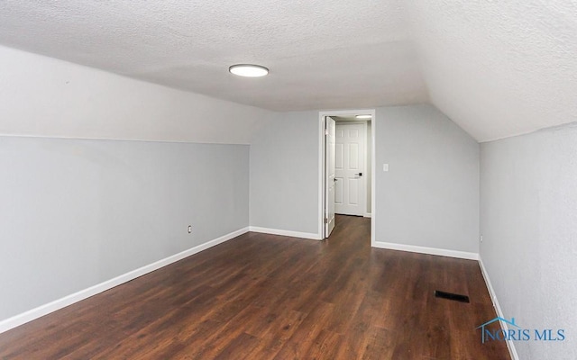 additional living space with vaulted ceiling, dark hardwood / wood-style floors, and a textured ceiling