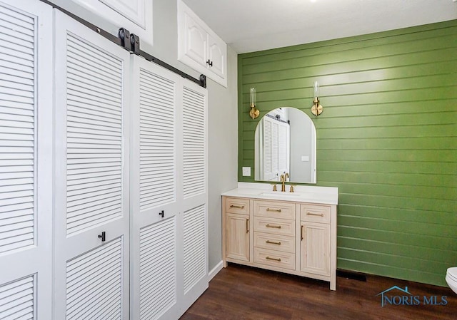 bathroom with hardwood / wood-style flooring, vanity, wooden walls, and toilet