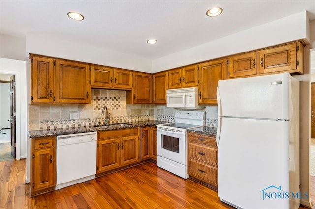 kitchen featuring tasteful backsplash, white appliances, dark wood-type flooring, sink, and dark stone countertops