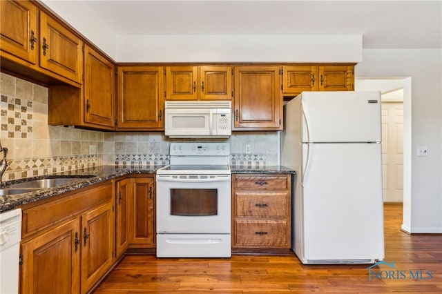 kitchen with white appliances, dark stone counters, sink, decorative backsplash, and light wood-type flooring