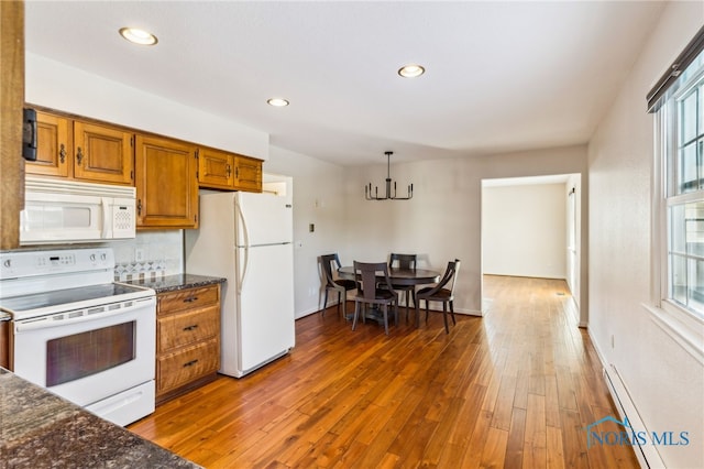 kitchen with dark stone counters, white appliances, dark wood-type flooring, decorative light fixtures, and a baseboard radiator