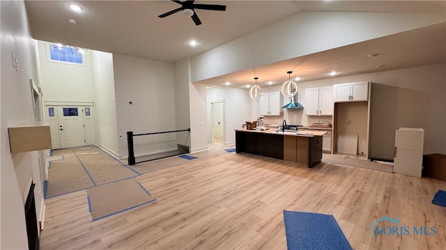 kitchen with high vaulted ceiling, white cabinets, hanging light fixtures, a kitchen island with sink, and light hardwood / wood-style flooring