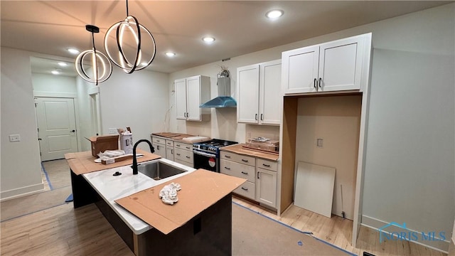 kitchen featuring pendant lighting, wall chimney range hood, white cabinetry, a center island with sink, and stainless steel range with gas cooktop