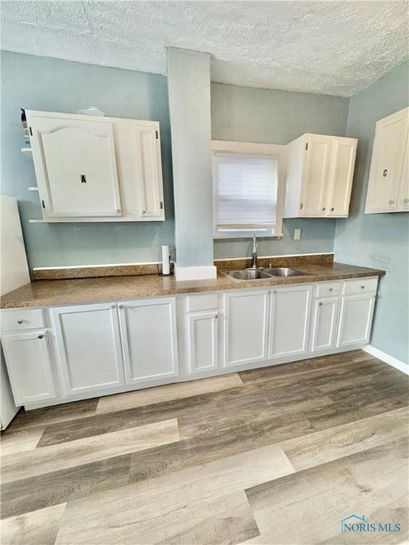 kitchen featuring white cabinets, light hardwood / wood-style flooring, sink, and a textured ceiling