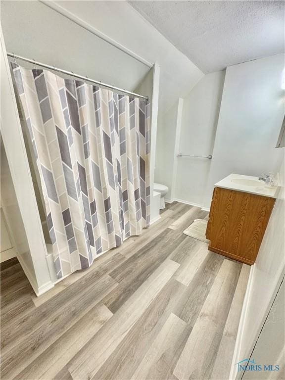 bathroom with hardwood / wood-style floors, vanity, vaulted ceiling, toilet, and a textured ceiling