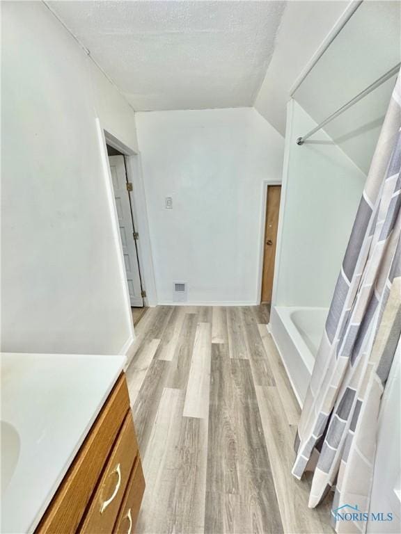 bathroom with vanity, lofted ceiling, hardwood / wood-style flooring, shower / bath combo with shower curtain, and a textured ceiling