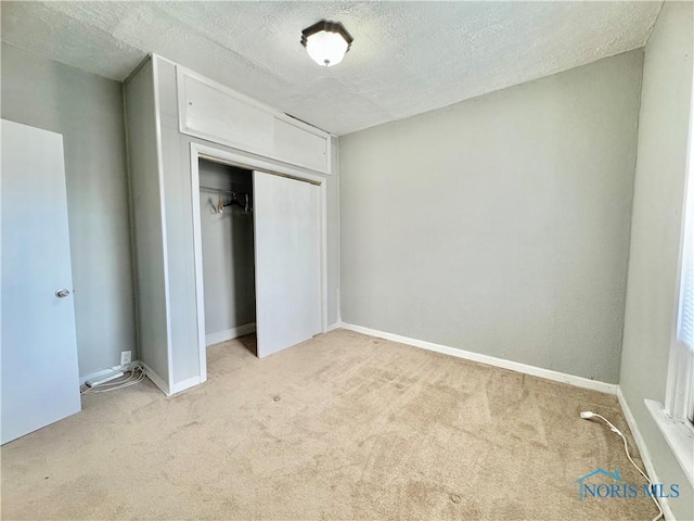 unfurnished bedroom featuring a textured ceiling, light colored carpet, and a closet