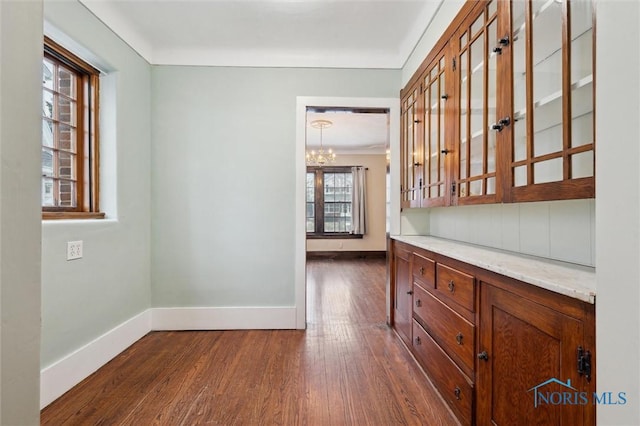 interior space with dark wood-type flooring, a chandelier, crown molding, and light stone countertops