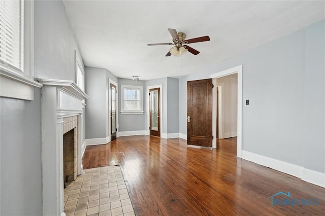 unfurnished living room featuring ceiling fan, a tiled fireplace, and light wood-type flooring