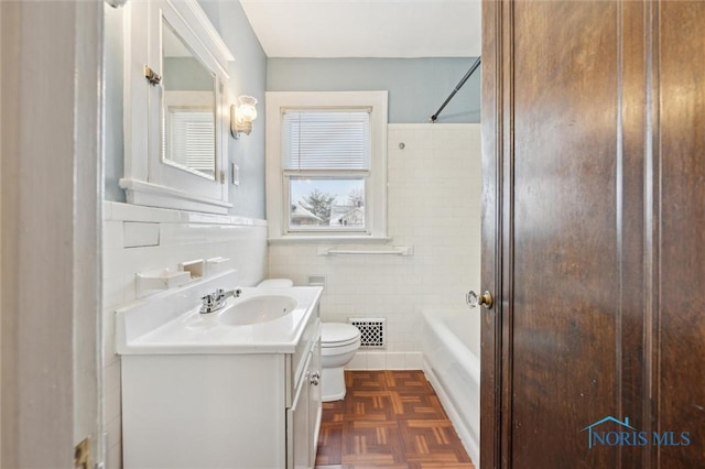 full bathroom with toilet, parquet flooring, tile walls,  shower combination, and vanity