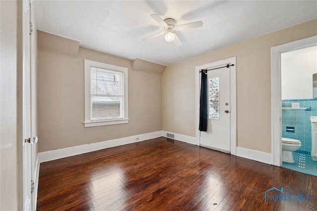 interior space with ceiling fan, tile walls, and dark wood-type flooring