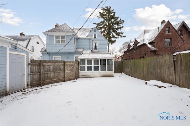 snow covered rear of property with a sunroom