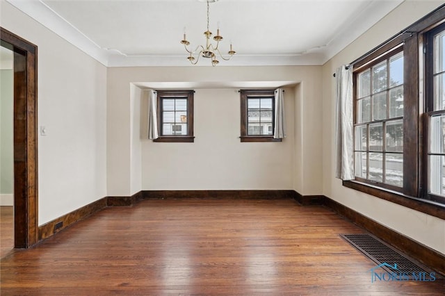 spare room featuring wood-type flooring, ornamental molding, and a chandelier