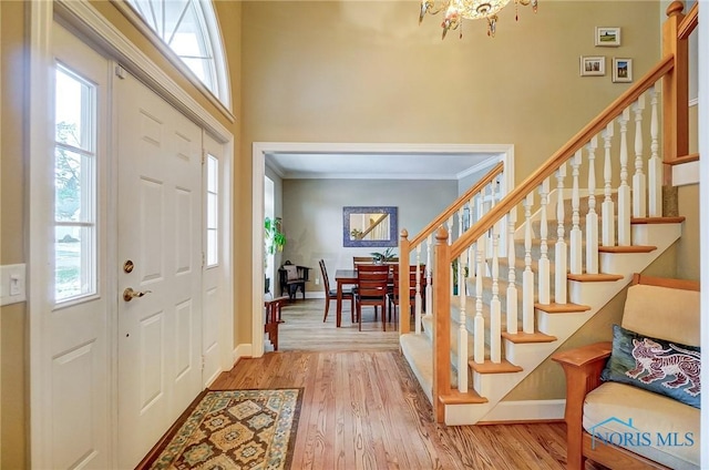 foyer entrance featuring crown molding, a towering ceiling, hardwood / wood-style floors, and a notable chandelier