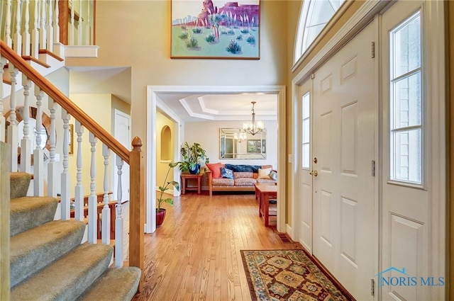 entryway with light hardwood / wood-style floors, a raised ceiling, and a chandelier