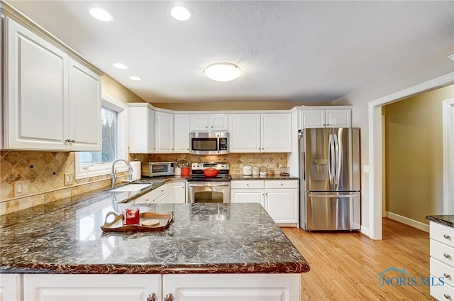 kitchen featuring sink, appliances with stainless steel finishes, tasteful backsplash, white cabinets, and dark stone counters