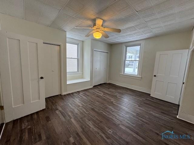 unfurnished bedroom with dark wood-type flooring, ceiling fan, and multiple closets