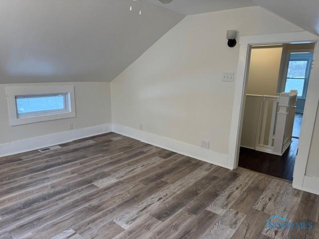 additional living space with dark hardwood / wood-style floors, a healthy amount of sunlight, and vaulted ceiling