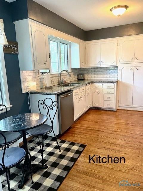 kitchen with sink, stainless steel dishwasher, dark stone countertops, light hardwood / wood-style floors, and white cabinetry