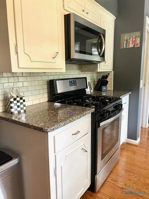 kitchen featuring light hardwood / wood-style floors, white cabinets, dark stone counters, and appliances with stainless steel finishes