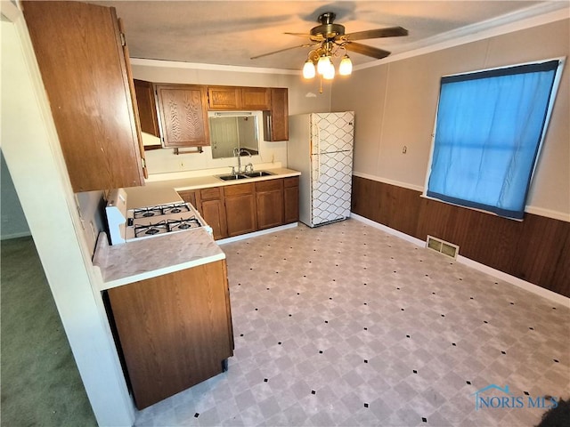 kitchen featuring ornamental molding, white appliances, ceiling fan, sink, and wood walls