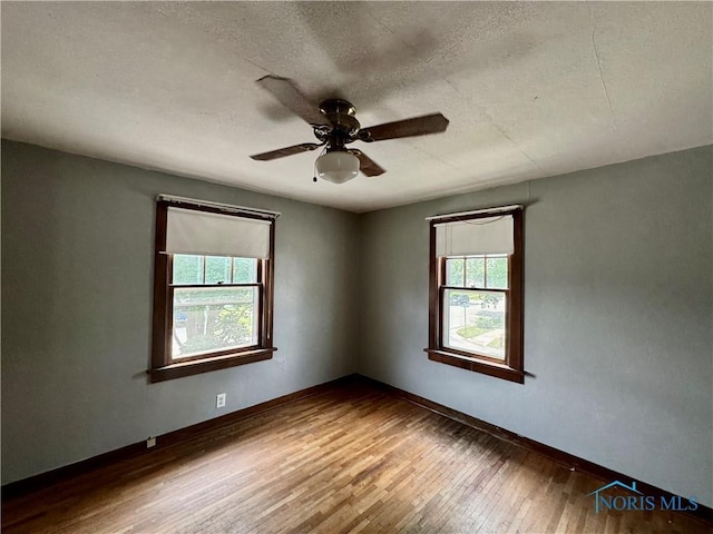 empty room with a wealth of natural light, ceiling fan, a textured ceiling, and hardwood / wood-style flooring