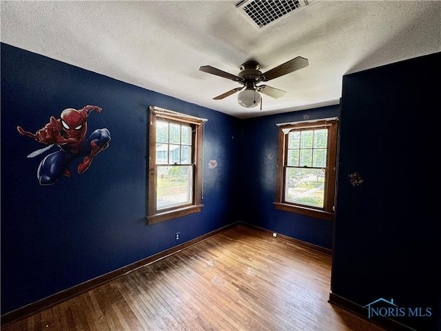 spare room featuring a healthy amount of sunlight, ceiling fan, wood-type flooring, and a textured ceiling