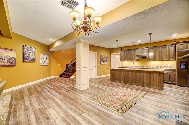 kitchen with stainless steel appliances, an inviting chandelier, light hardwood / wood-style floors, decorative light fixtures, and a center island with sink