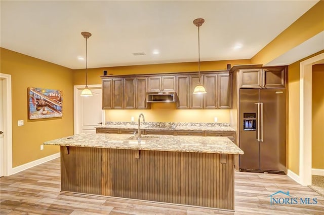 kitchen featuring appliances with stainless steel finishes, decorative light fixtures, a kitchen island with sink, and sink