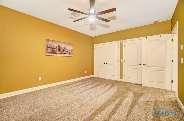 unfurnished bedroom with ceiling fan, carpet floors, and two closets