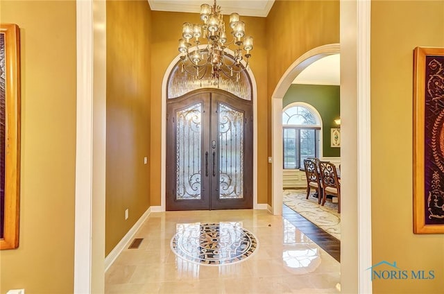 foyer entrance with french doors, ornamental molding, and a notable chandelier