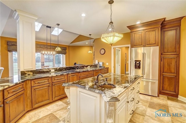 kitchen with high end fridge, kitchen peninsula, hanging light fixtures, and dark stone counters