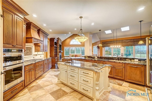 kitchen with light stone countertops, lofted ceiling with skylight, an island with sink, and hanging light fixtures