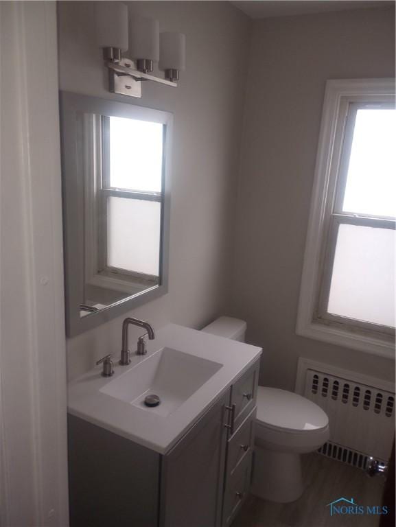 bathroom with hardwood / wood-style flooring, vanity, toilet, and radiator