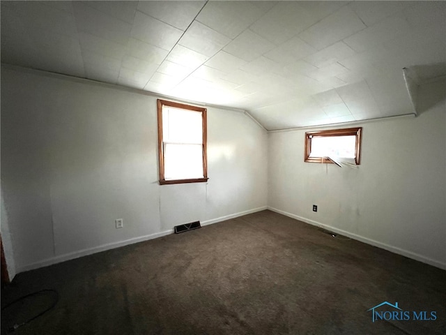 additional living space with a healthy amount of sunlight, vaulted ceiling, and dark carpet