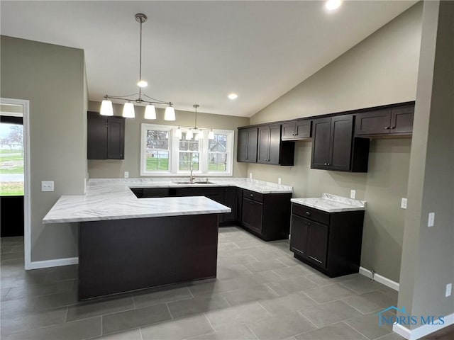 kitchen featuring kitchen peninsula, light stone counters, sink, decorative light fixtures, and lofted ceiling