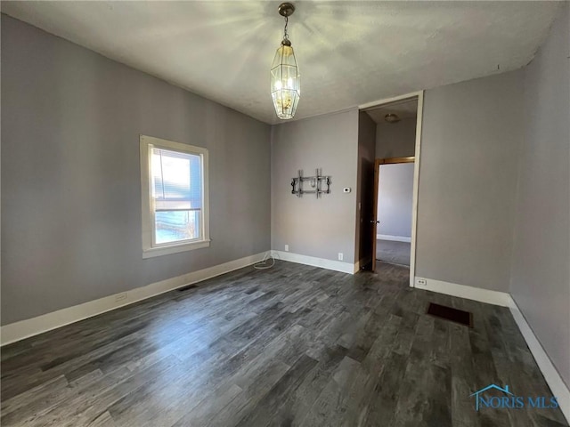 empty room featuring dark hardwood / wood-style floors and a notable chandelier