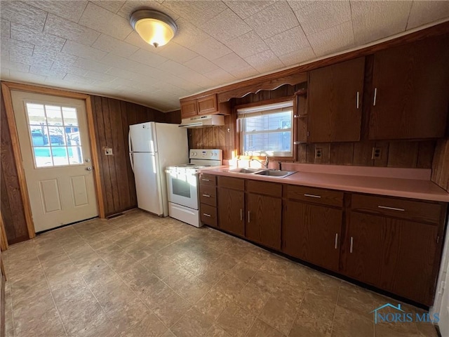 kitchen with vaulted ceiling, wood walls, sink, and white appliances