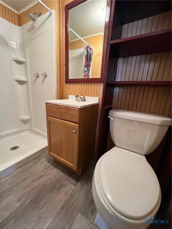 bathroom with ornamental molding, vanity, a shower, wood-type flooring, and toilet